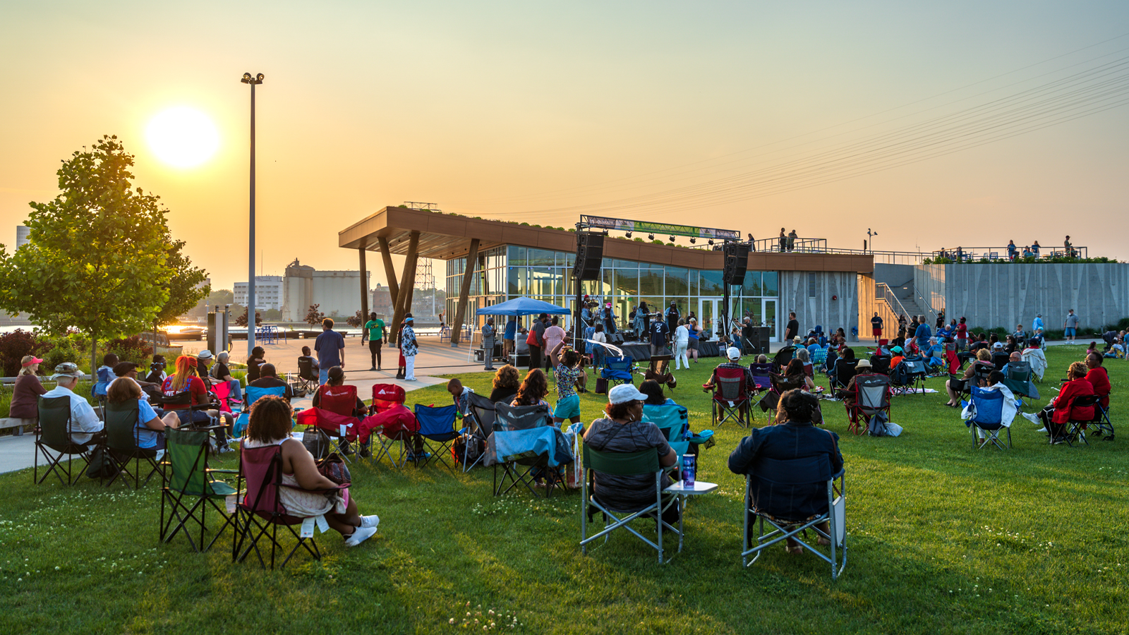 glass city jazz fest at Glass City metroapark. The sun is setting and people are sitting in bag chairs listening to music.