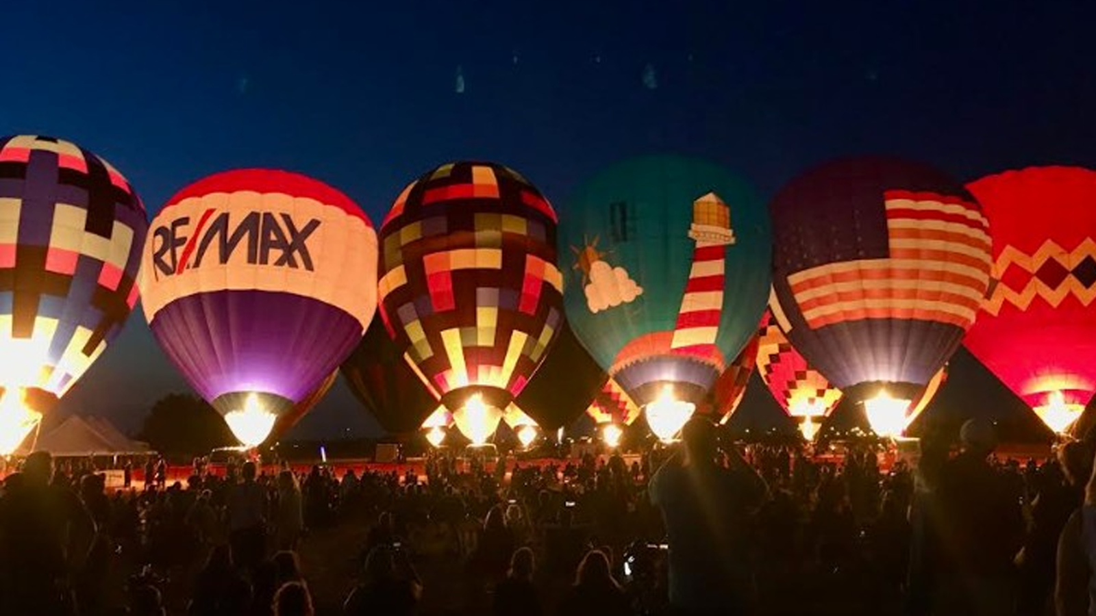 Hot air balloons outside at night getting ready to take off. There is a crowd of people watching.