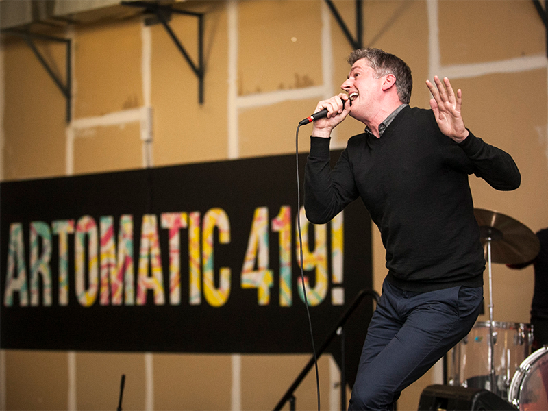a man singing on stage with an "artomatic 419" sign in the background