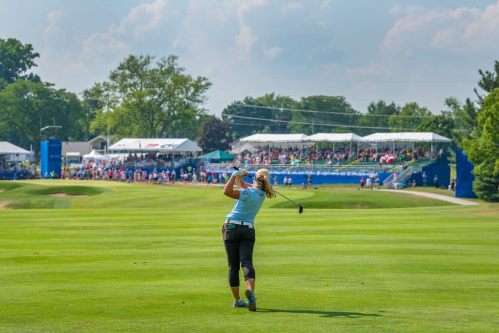 Golfer swinging with crowd and stands in the distance at Dana Open golf tournament